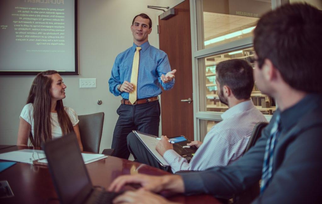 4 people in a conference room, with 1 of them standing and presenting to the others